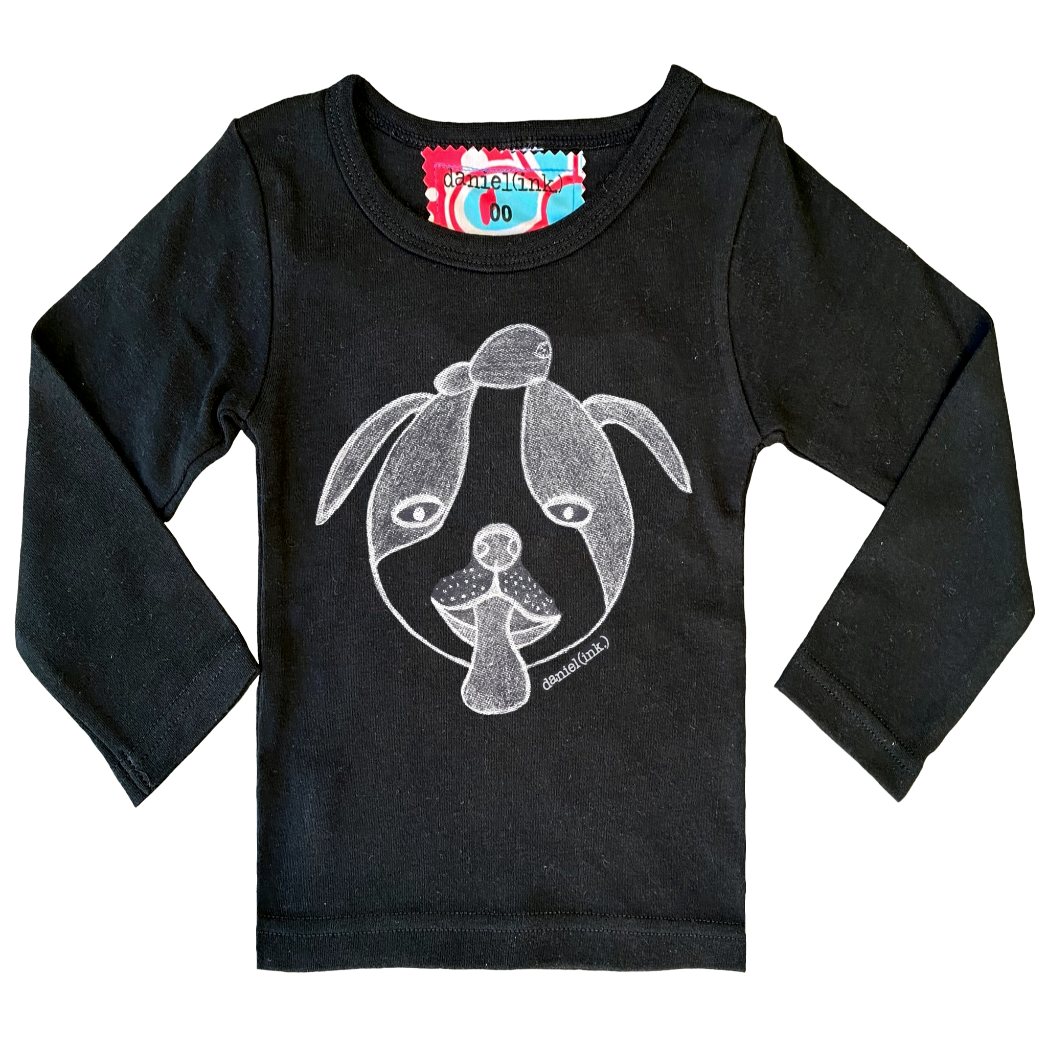 Black long sleeve babies’ shirt featuring a hand drawn sketch of a dog’s face in white. The dog has a round head, floppy ears, wide eyes, and its tongue is sticking out. There is also a red, white, and blue fabric label on the back of the neck. 