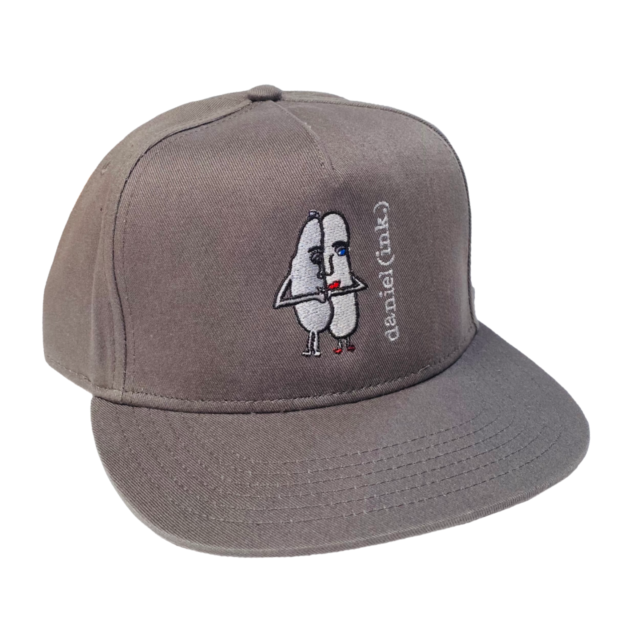 Storm snapback cap featuring an embroidered image of two oval-shaped humanoid figures merged side by side and holding hands in silver. The humanoid figure on the left is wearing a bowler hat and the humanoid figure on the right has red lips. The name daniel(ink.) is embroidered in silver thread next to the oval-shaped humanoid figures. 